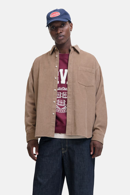 Chemise brune à manches longues d'ORIGINALS BY JACK & JONES, en texture corduroy, portée sur un pull bordeaux avec imprimé et des jeans bleus foncés.