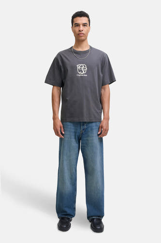 T-shirt gris à manches courtes d'ORIGINALS BY JACK & JONES, avec un logo blanc sur la poitrine, porté avec une chaîne argentée et des jeans larges.
