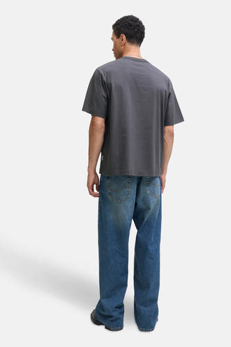T-shirt gris à manches courtes d'ORIGINALS BY JACK & JONES, avec une coupe décontractée et associé à des jeans larges et des chaussures noires.