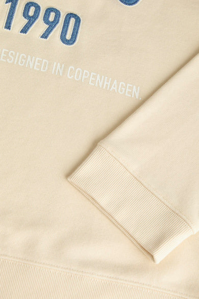 Gilet beige d'ORIGINALS BY JACK & JONES, avec le texte "Conçu en 1990 à Copenhague" et un bord côtelé aux manches.
