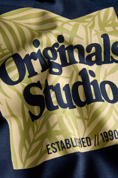 T-shirt bleu à manches courtes d'ORIGINALS BY JACK & JONES, avec un motif de feuilles tropicales et le texte 'Originals Studio Established // 1990'.