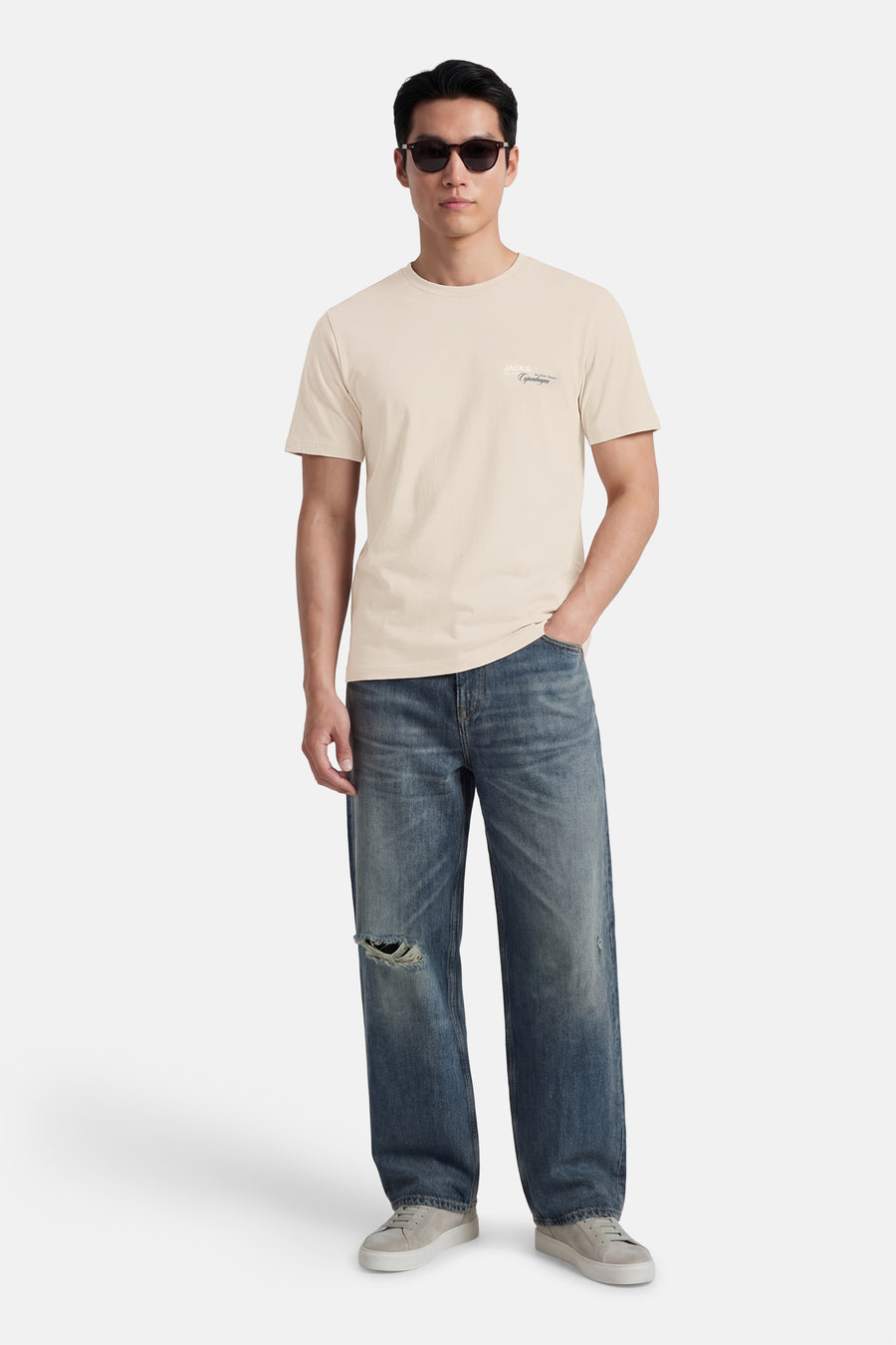 Beige T-shirt met korte mouwen van CORE BY JACK & JONES, gedragen met blauwe jeans met scheuren en grijze sneakers.