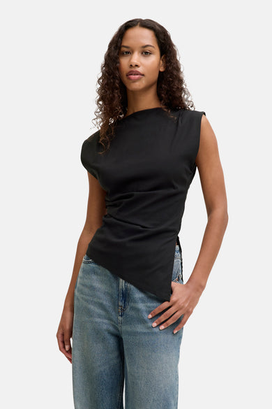 Blouse no manches noire de JJXX, avec un col asymétrique et associée à des jeans larges.