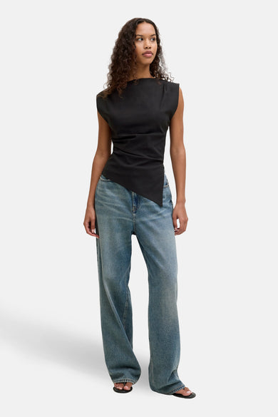 Mouwloze zwarte blouse van JJXX, met asymmetrisch gesneden zoom en gecombineerd met wijde jeans.
