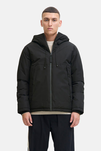 Veste courte noire de CORE BY JACK & JONES avec capuche et logo blanc sur la manche, portée par un homme de profil.