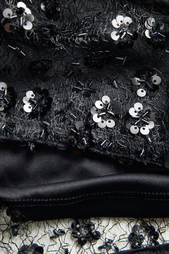 Blouse noire de JJXX avec un motif floral en paillettes et perles sur un tissu transparent.
