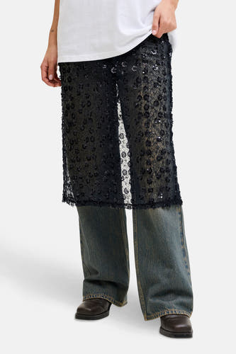 Longue jupe noire de JJXX, avec motif floral et paillettes, associée à une chemise blanche, des jeans et des chaussures marrons.