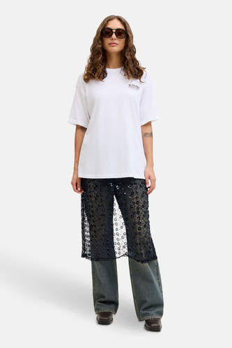 Longue robe noire de JJXX, avec un motif floral et des paillettes, portée sur un jean bleu.