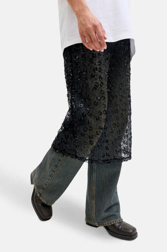 Longue jupe noire de JJXX, en tissu transparent avec motif floral et paillettes, portée sur un jean bleu.