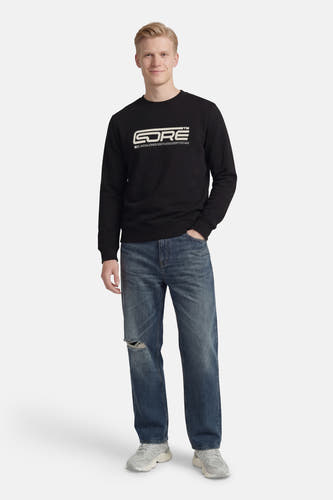 Zwarte sweater van CORE BY JACK & JONES, met witte logo-opdruk, gedragen met blauwe jeans met scheuren en grijze sneakers.