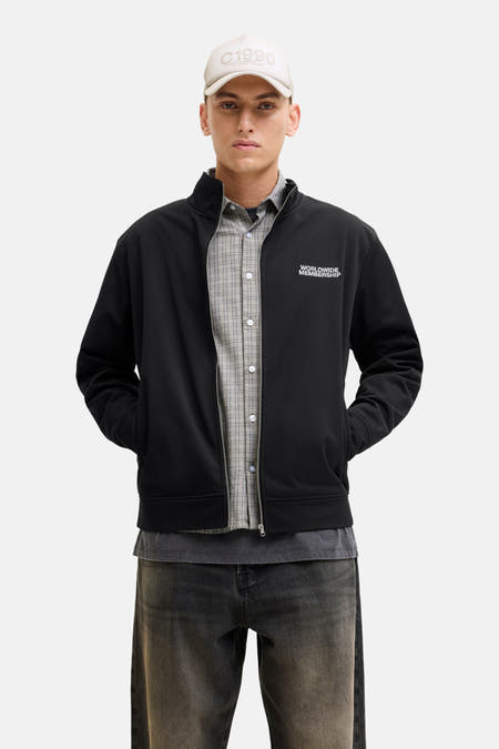 Gilet noir de CORE BY JACK & JONES, porté sur une chemise à carreaux, avec un chapeau coordonné et des jeans foncés.