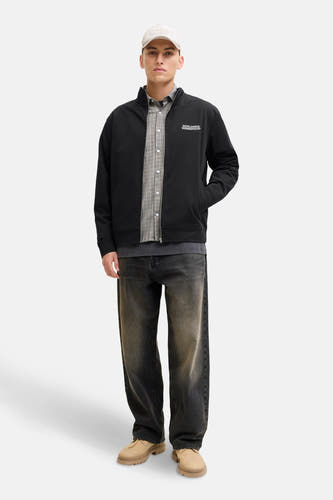 Gilet noir de CORE BY JACK & JONES, porté sur un chemisier à carreaux avec des jeans foncés et un chapeau.