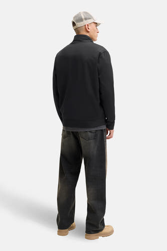Gilet noir de CORE BY JACK & JONES, vu de l'arrière, avec un chapeau beige et des jeans larges.