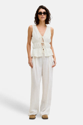 Witte mouwloze blouse van JJXX met striksluiting en peplumzoom, gedragen met gestreepte broek en zonnebril.