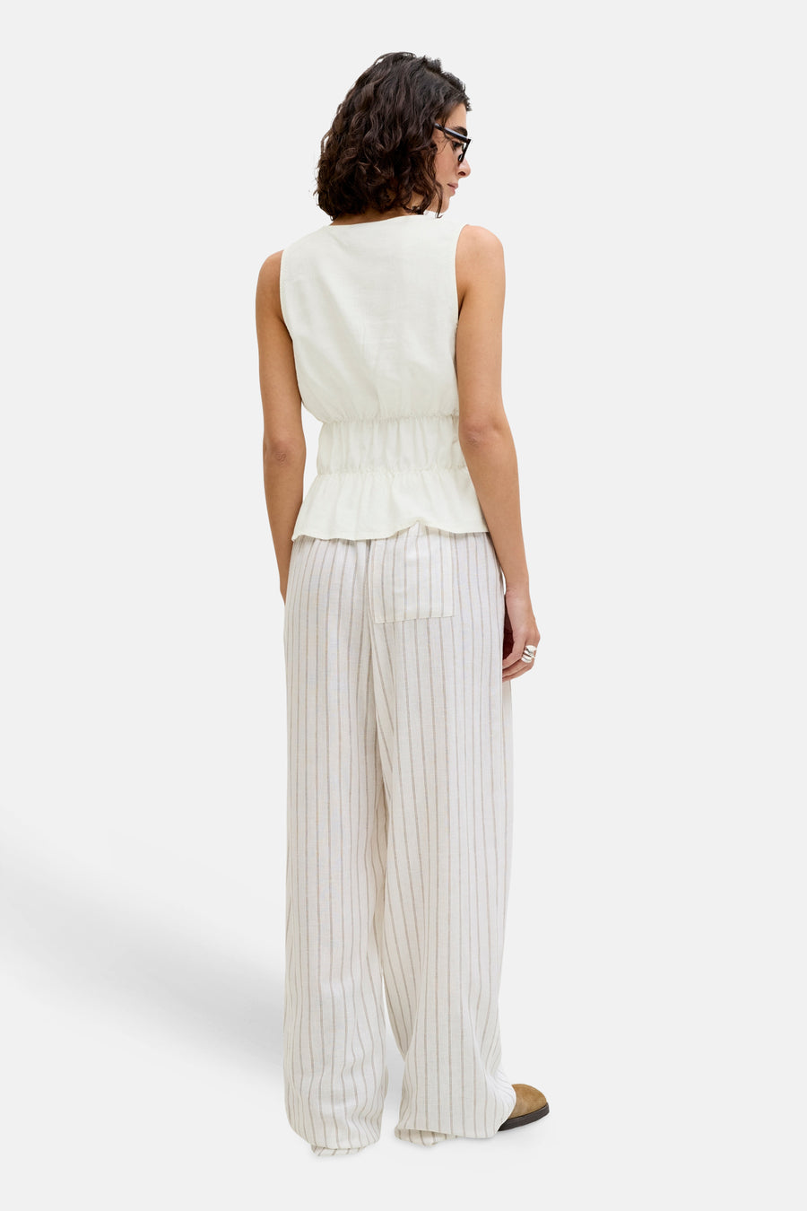 Chemisier blanc sans manches de JJXX avec taille plissée, vu de dos sur un pantalon rayé.