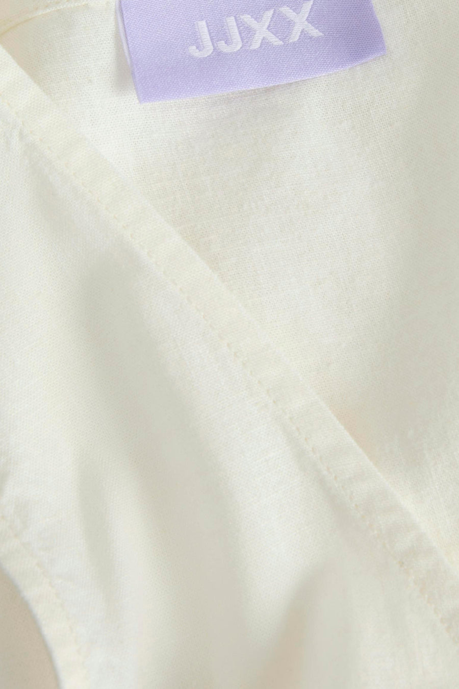 Chemisier blanc de JJXX avec une étiquette légèrement violette et des surpiqûres visibles, en gros plan.