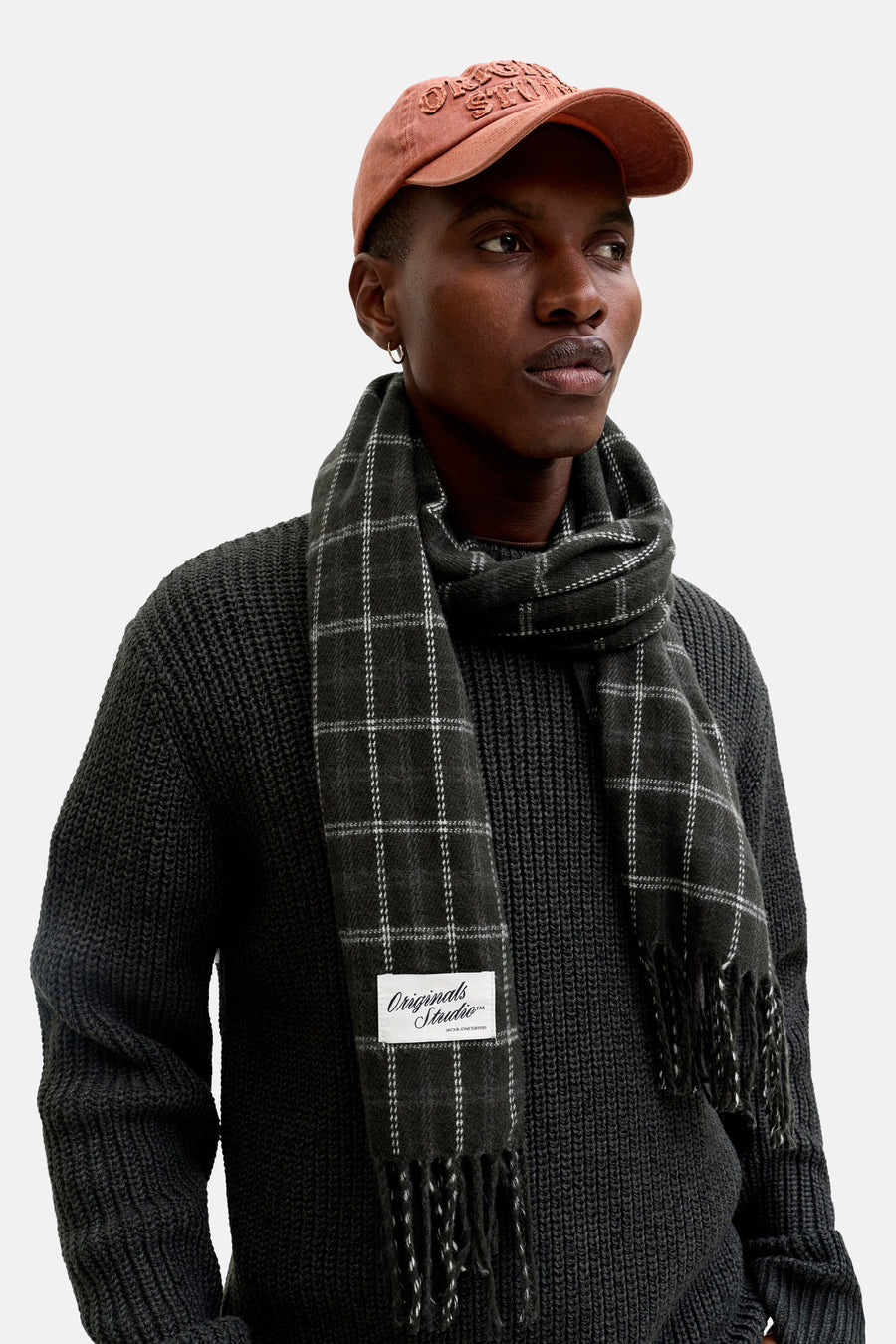 Een man met een donkergrijze trui en geruite sjaal, met een oranje pet.