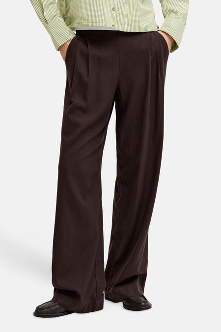 Pantalon marron de JJXX, à jambes larges et taille plissée, combiné avec une chemise à carreaux vert et blanc.