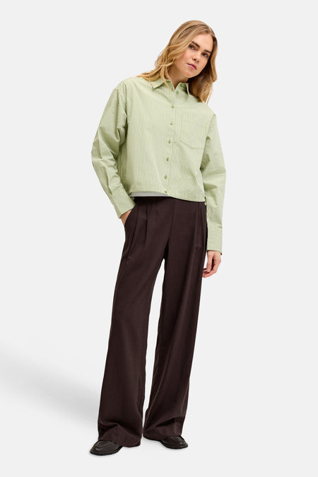 Bruine broek van JJXX, met wijde pijpen en een geplooide taille, gecombineerd met een groen-wit geruit overhemd.
