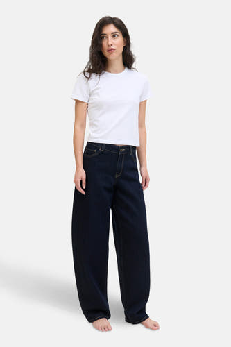 Jean en denim bleu marine spécial fit de JJXX, porté avec un T-shirt blanc et pieds nus.