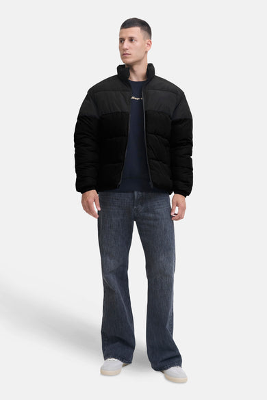 Manteau court noir de CORE BY JACK & JONES, avec un design matelassé, porté avec des jeans noirs et des baskets blanches.