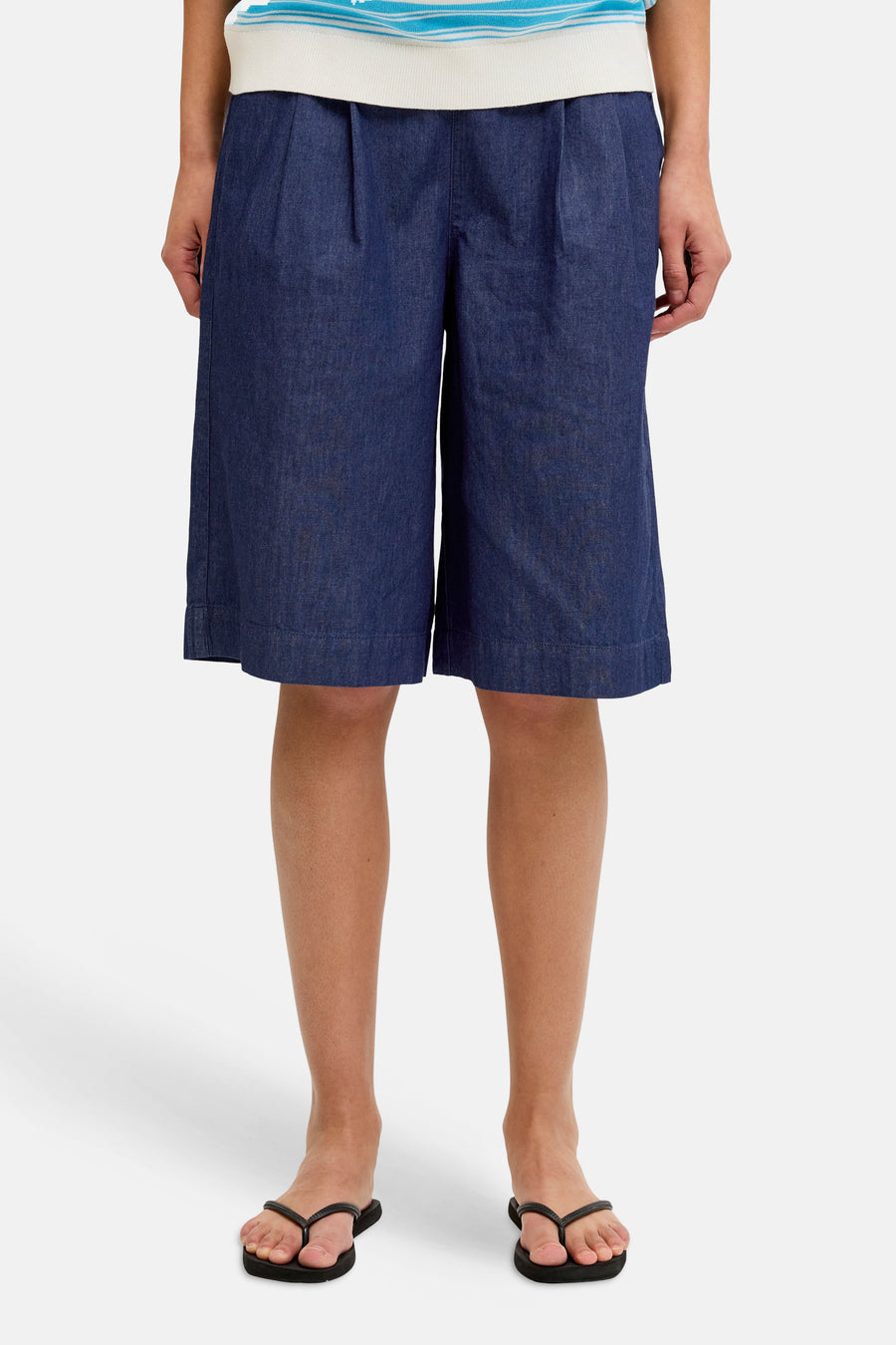 Short en jean bleu marine JJXX à jambes larges et plis, porté avec un polo rayé et des tongs.