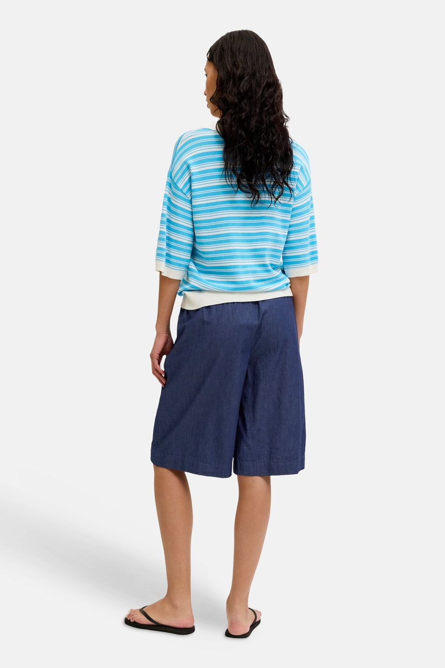 Short en jean bleu marine JJXX, coupe ample, longueur genou, dos, porté avec un t-shirt rayé et des tongs noires.