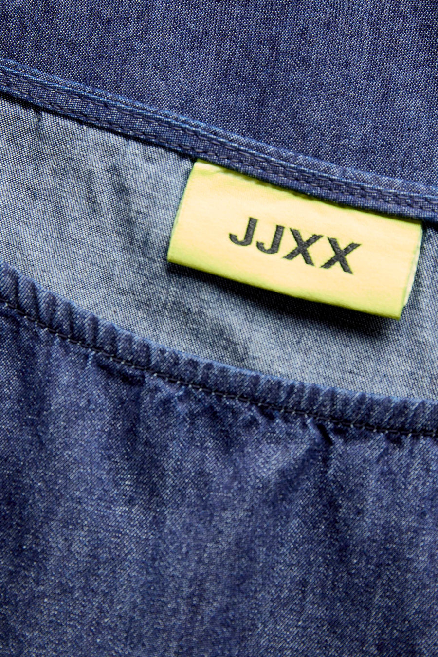 Chemise en jean bleu foncé de JJXX avec texture fine, surpiqûres visibles et une étiquette jaune.