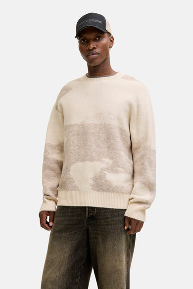 Gilet beige à col rond de CORE BY JACK & JONES, porté sous un gilet kaki avec capuchon, associé à des jeans noirs et des baskets marrons.