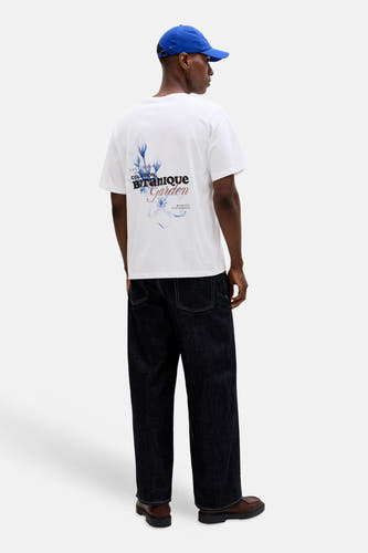 T-shirt blanc à manches courtes de ORIGINALS BY JACK & JONES, avec imprimé botanique au dos, porté avec une casquette bleue et un jean ample foncé.