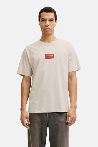 T-shirt beige à manches courtes de CORE BY JACK & JONES, avec un écusson rouge sur la poitrine.