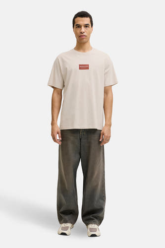 T-shirt beige à manches courtes de CORE BY JACK & JONES, porté avec un jean ample et des baskets.