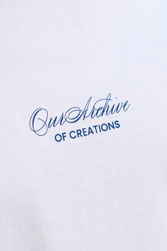 T-shirt blanc ORIGINALS BY JACK & JONES avec imprimé bleu 'Our Archive OF CREATIONS' sur le tissu blanc, gros plan.