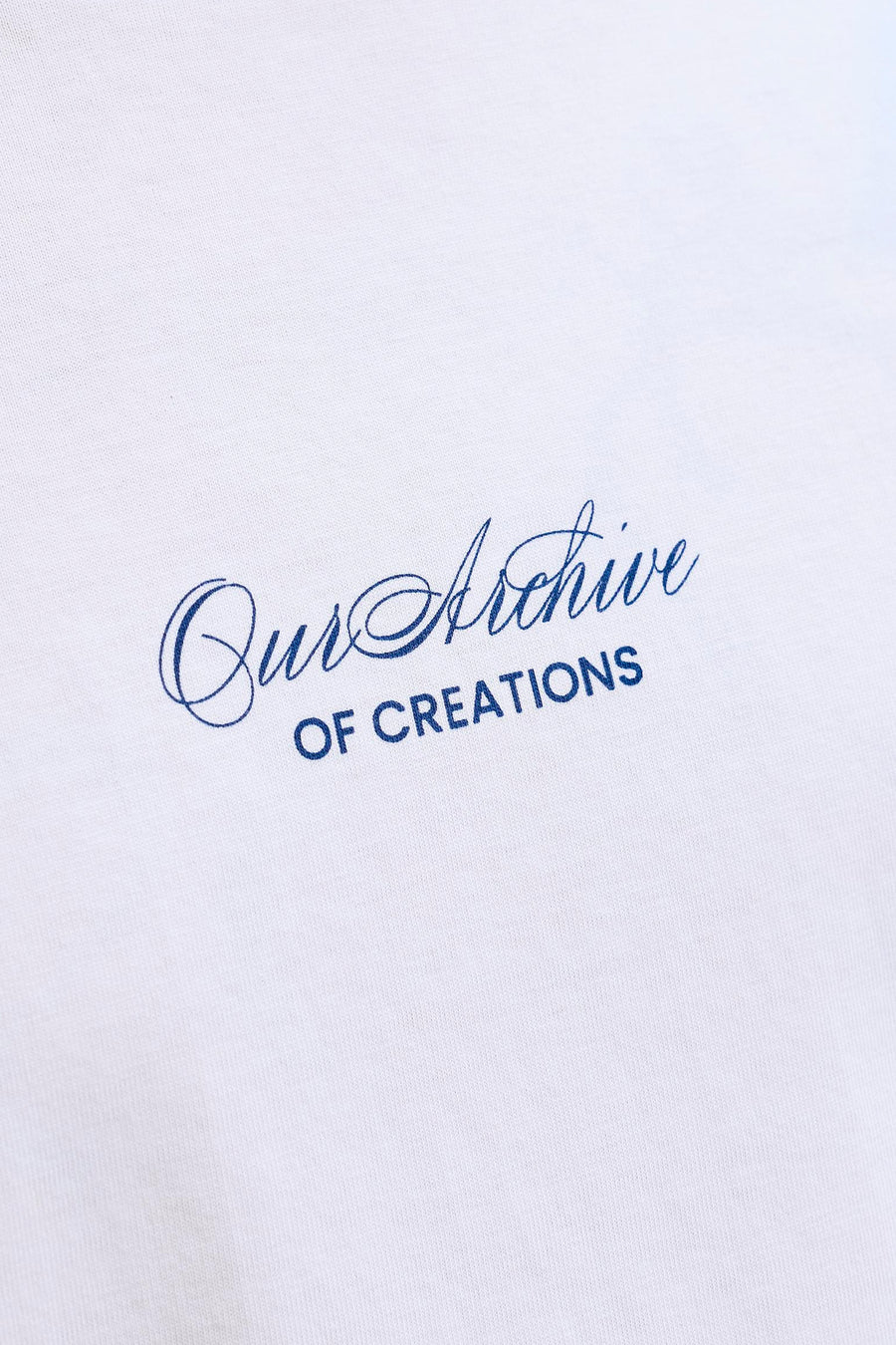 T-shirt blanc ORIGINALS BY JACK & JONES avec imprimé bleu 'Our Archive OF CREATIONS' sur le tissu blanc, gros plan.
