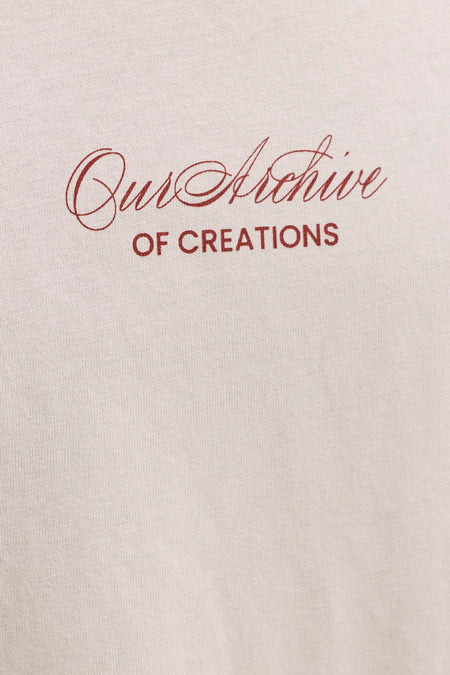 T-shirt beige de ORIGINALS BY JACK & JONES avec texte rouge 'Our Archive OF CREATIONS' sur un tissu tricoté.