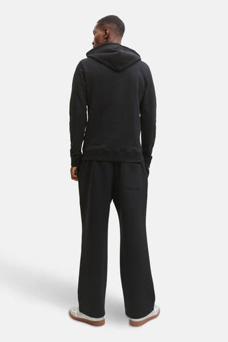 Pull-over noir avec capuche de CORE BY JACK & JONES, vu de dos, avec des pantalons noirs correspondants et des chaussures blanches à semelles brunes.