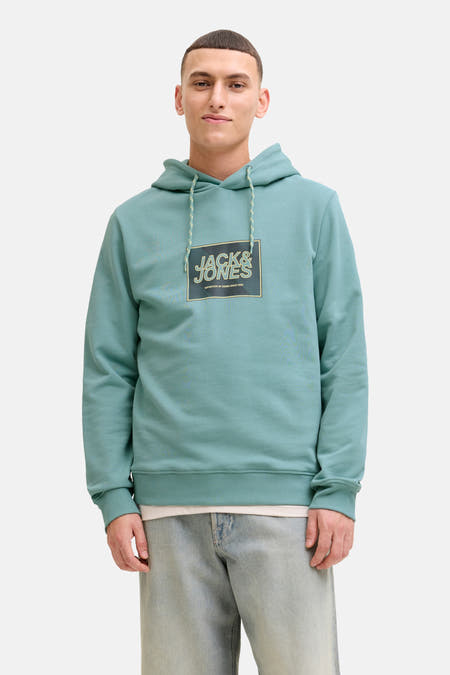 Pull-over vert de CAP par CORE by JACK & JONES, avec un logo sur la poitrine, associé à des jeans bleus et des chaussures blanches.