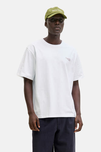 T-shirt blanc à manches courtes d'ORIGINALS BY JACK & JONES, avec une petite impression textuelle sur la poitrine, associé à un pantalon bleu et des chaussures marrons.