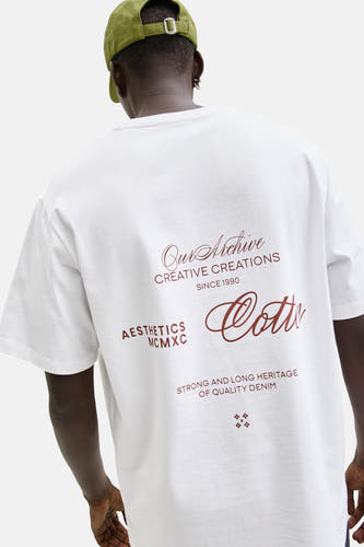 T-shirt blanc à manches courtes d'ORIGINALS BY JACK & JONES, avec un imprimé sur le dos et porté avec une casquette verte.