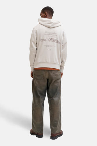 Gilet beige avec capuche d'ORIGINALS BY JACK & JONES, avec un message sur le dos, associé à une chemise orange et des jeans marrons.