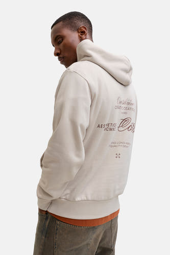 Gilet beige avec capuche d'ORIGINALS BY JACK & JONES, imprimé sur le dos, associé à des jeans marrons.