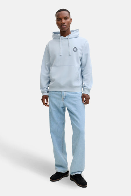 Man met lichtblauwe hoodie en jeans, staand.