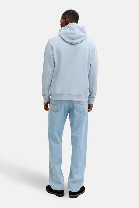 Man van achteren, blauwe hoodie en jeans, zwarte schoenen.
