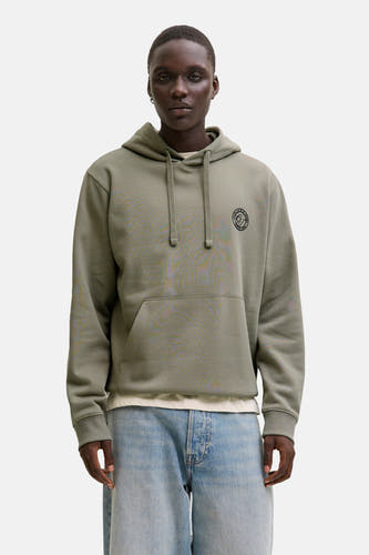 Gilet kaki avec un chapeau d'ORIGINALS BY JACK & JONES, avec une poche kangourou et des cordons, porté avec des jeans bleus.