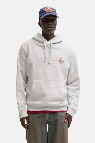 Pull-over blanc avec capuche d'ORIGINALS BY JACK & JONES, porté sous un manteau de denim foncé et une casquette bleue.
