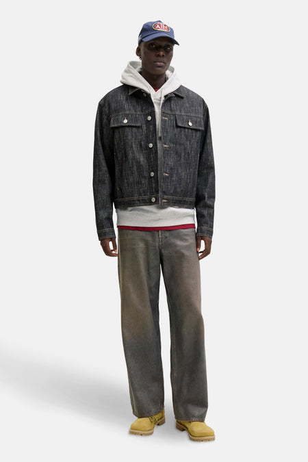 Man met pet, spijkerjas, hoodie, wijde broek en gele schoenen.