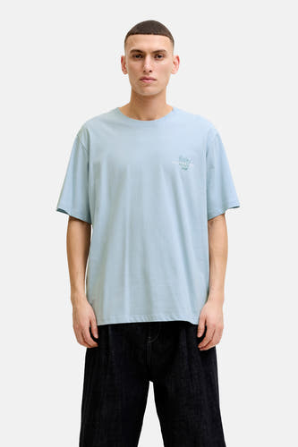 T-shirt bleu de ORIGINALS BY JACK & JONES avec imprimé discret sur la poitrine, porté avec un short foncé et des baskets blanches.