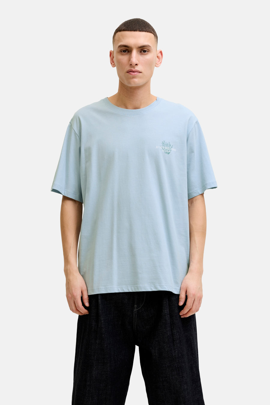 T-shirt bleu de ORIGINALS BY JACK & JONES avec imprimé discret sur la poitrine, porté avec un short foncé et des baskets blanches.