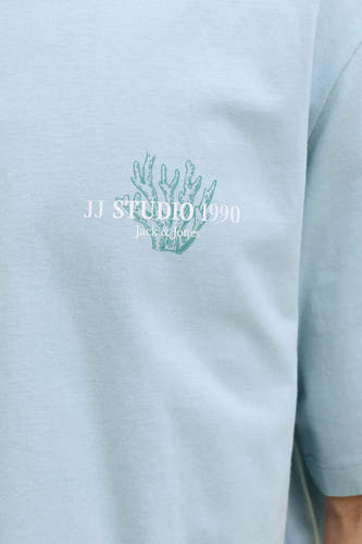 T-shirt en maille bleu de Jack & Jones avec un motif de corail vert et le texte 'JJ Studio 1990'.