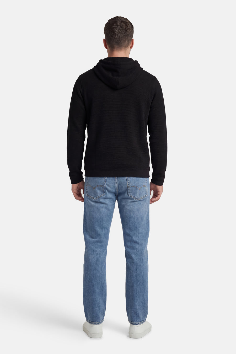 Zwarte sweater met kap van CORE BY JACK & JONES, achterkant, gecombineerd met blauwe jeans en witte sneakers.
